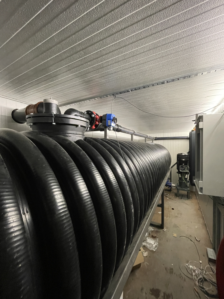 Stor rillet plasttank med rør og ventiler i et teknisk rom
