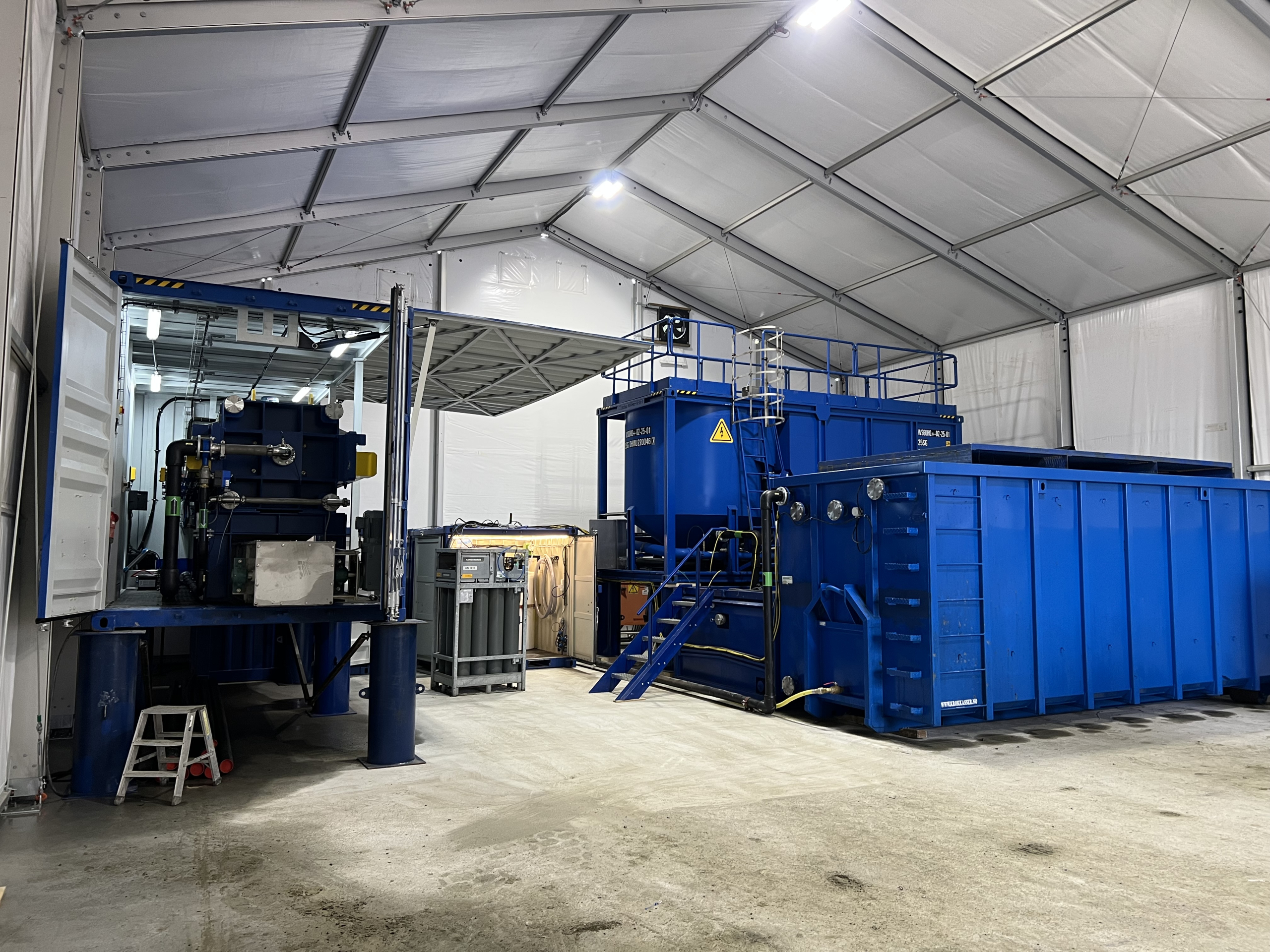 Blått industrielt utstyr og store tanker montert inne i et hvitt industritelt